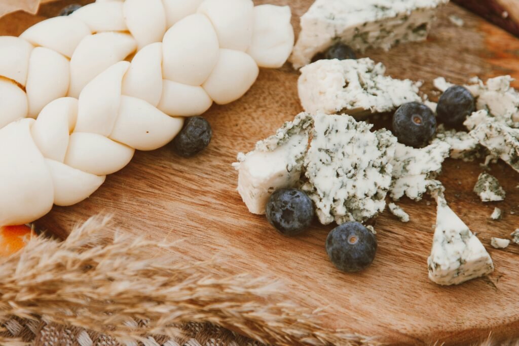 A rustic arrangement of blue cheese, braided cheese, and fresh blueberries on a wooden board.