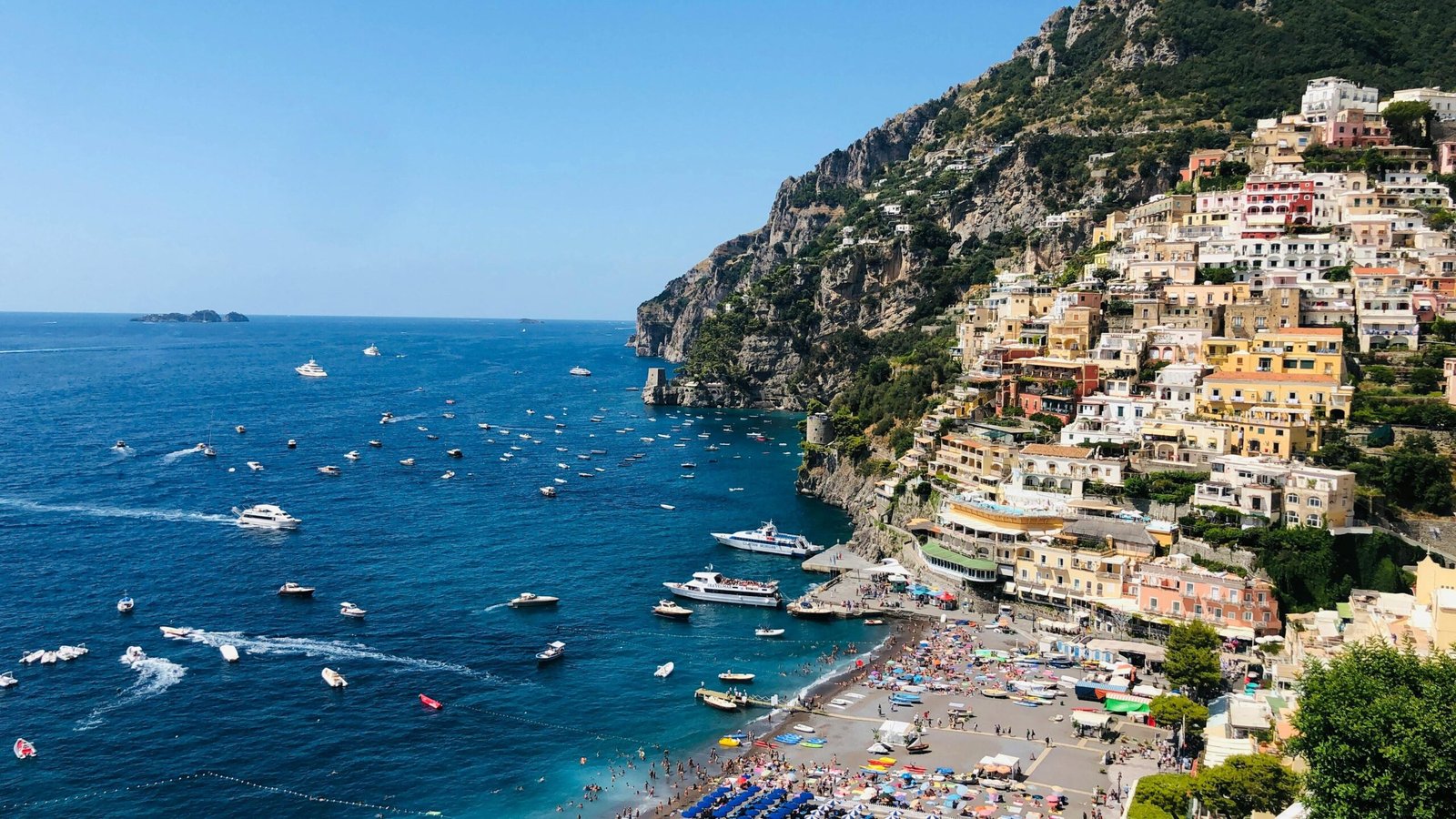 Scenic view of Amalfi Coast settlement located on green cliff near picturesque blue sea with floating boats on sunny summer day