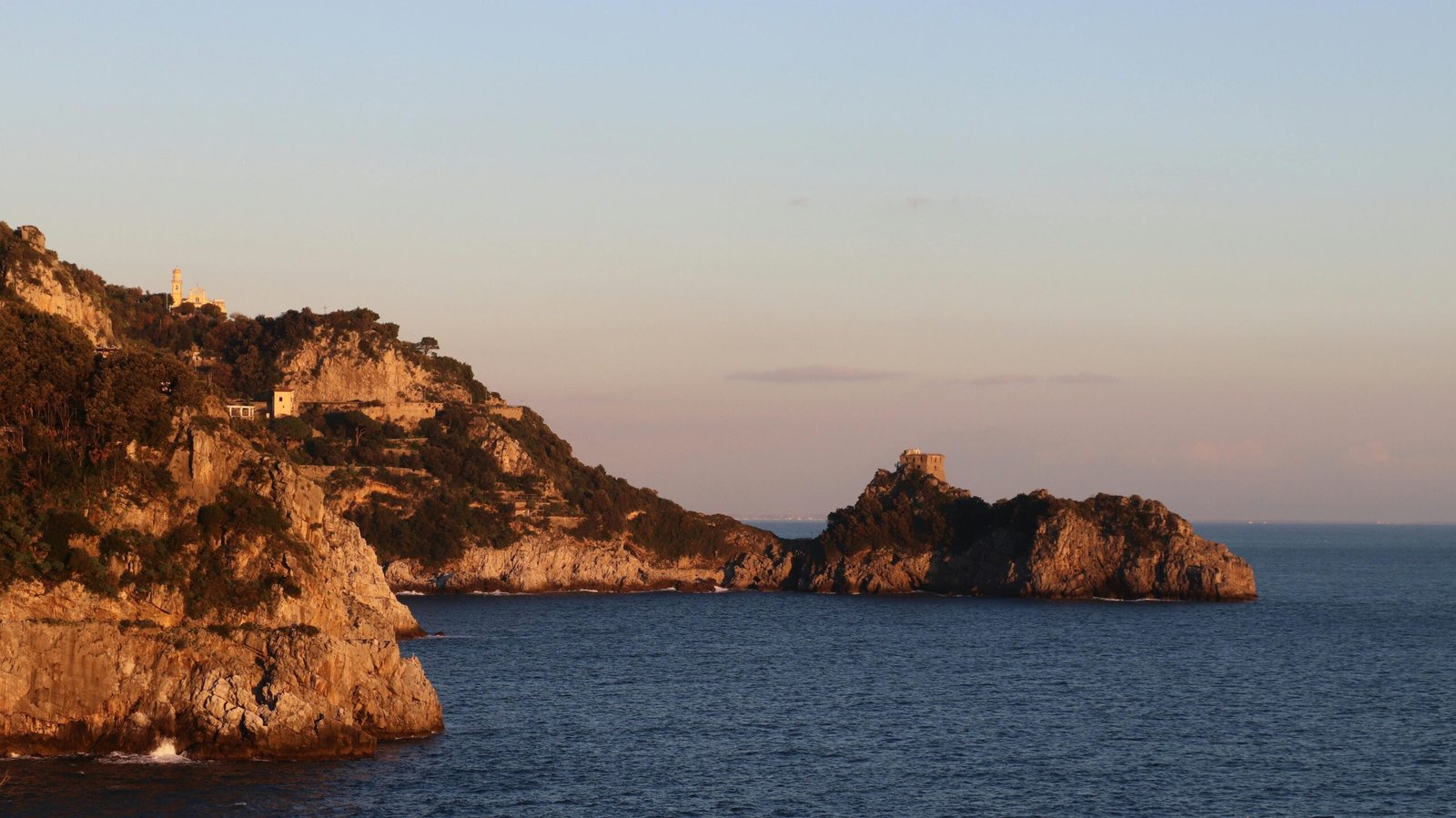 Dramatic cliffs meet tranquil sea at Praiano's coastline during sunset.