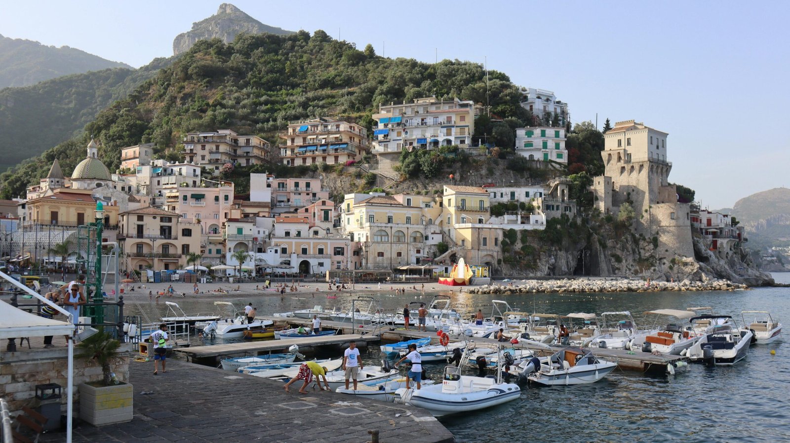 Boats moored at picturesque Amalfi coastline harbor in Italy with hillside houses and clear skies.